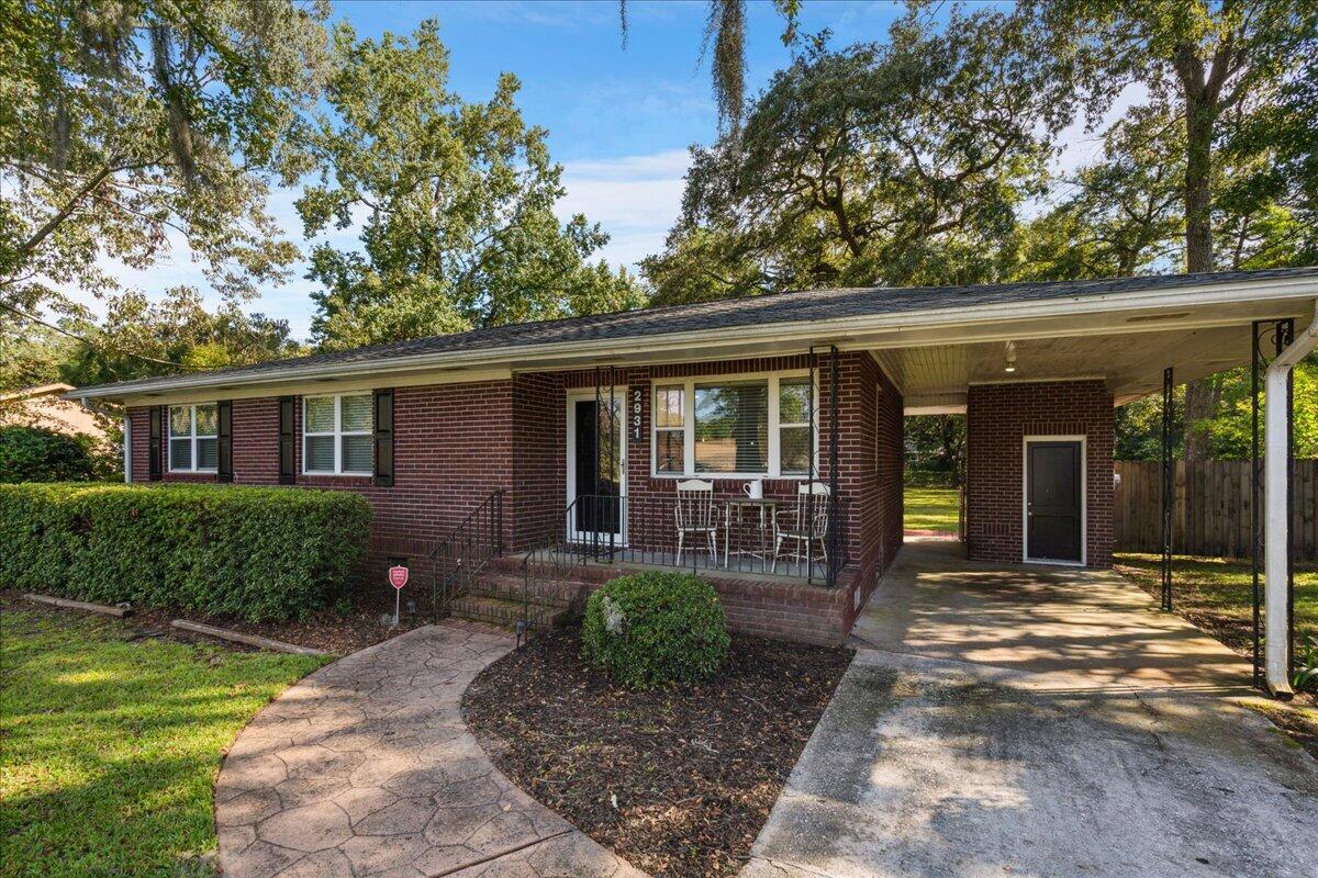 Brick ranch home with a covered carport, front patio, and mature shade trees.