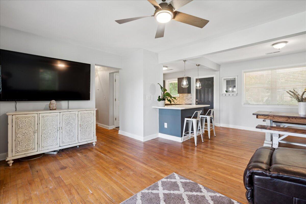 Open living room and kitchen with hardwood floors, a blue island, and a large wall-mounted television.