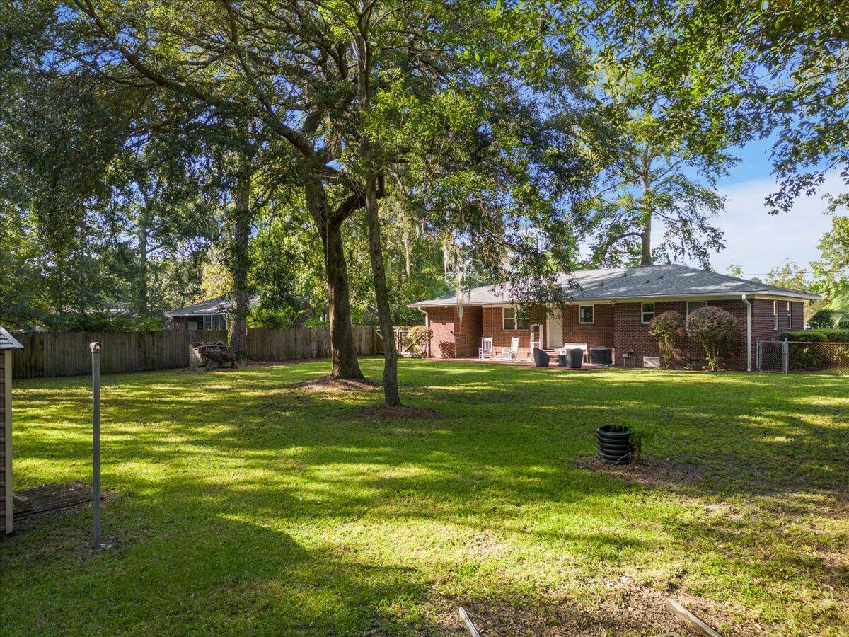 Brick home behind a spacious lawn, with mature shade trees and patio seating.