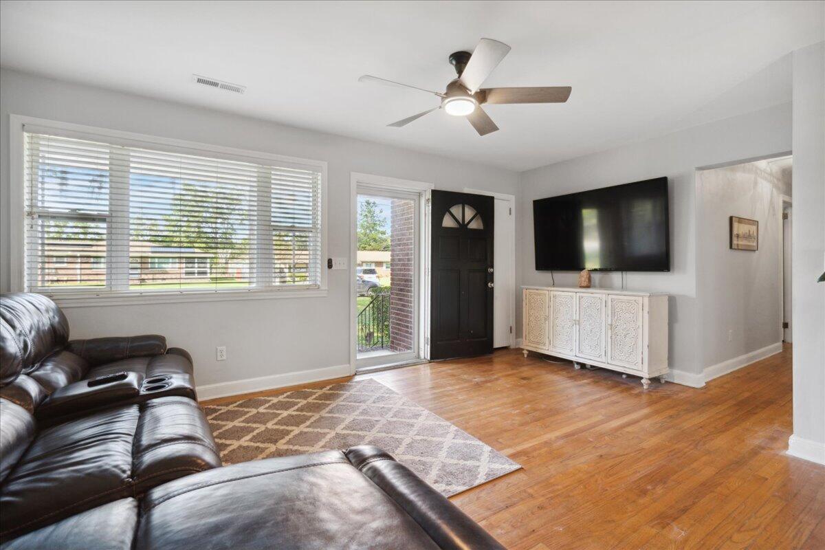 Living room with hardwood floors, a black leather sectional, and a large window with blinds.