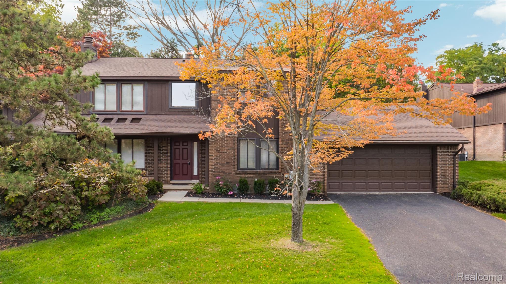 Two-story brick house with an attached garage beneath orange autumn foliage.