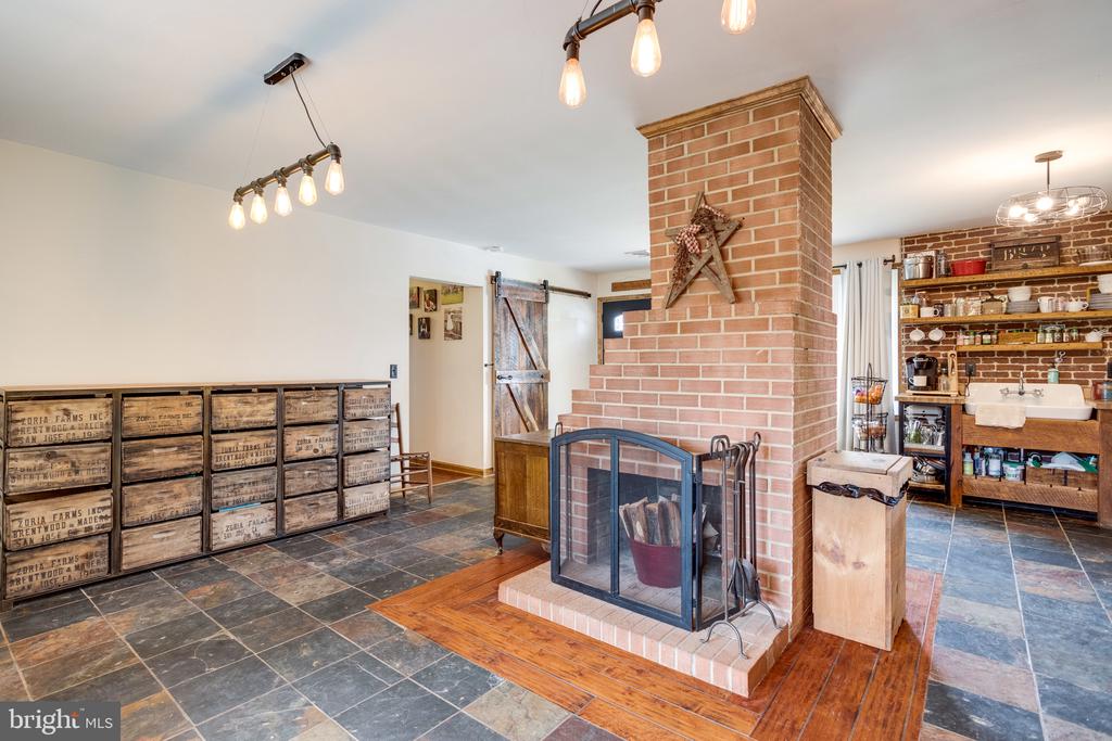 Rustic kitchen and living area with a brick fireplace, open shelving, and a farmhouse sink.