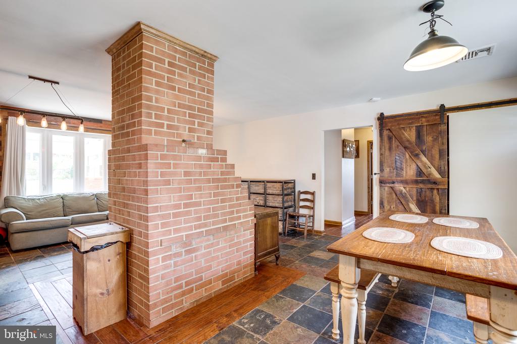 Dining area with a large brick chimney, wooden table, slate flooring, and rustic sliding barn door.