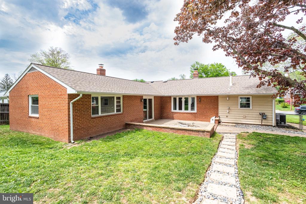 Rear of a single-story brick home with a raised patio and stone walkway across the lawn.