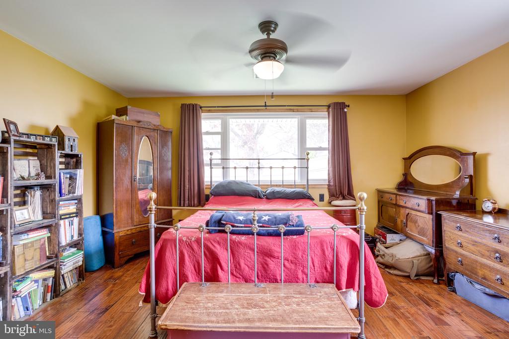 Bedroom with a red-covered metal bed, mustard-yellow walls, and wooden furniture.