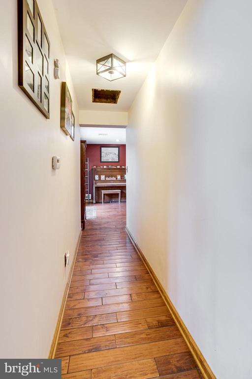 Long hallway with wood plank floors, framed wall art, and a red-walled room at the far end.