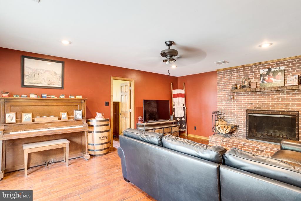 Living room with a brick fireplace, piano, hardwood floors, and black leather sectional.