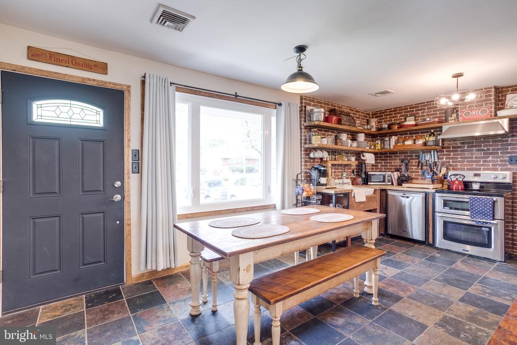 Kitchen with exposed brick walls, open shelves, stainless steel appliances, and a large wooden table.
