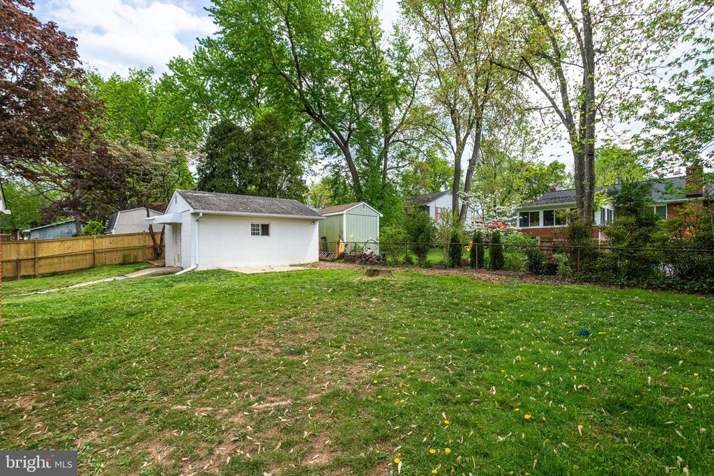 Backyard with a broad lawn, white detached garage, green shed, and mature trees.
