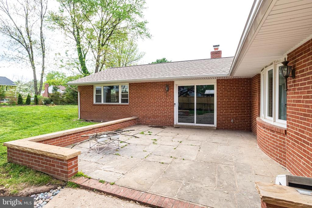 Rear brick patio with sliding glass doors, a low brick wall, and adjoining lawn.