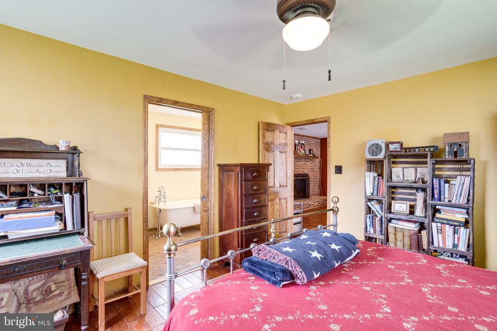 Bedroom with a red floral bedspread, yellow walls, dark wood furniture, and an open doorway to a clawfoot tub.