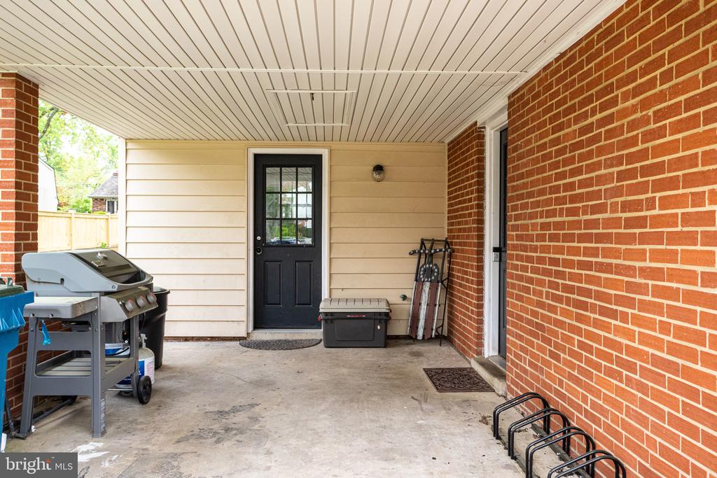 Covered patio with brick walls, a black entry door, and a barbecue grill.