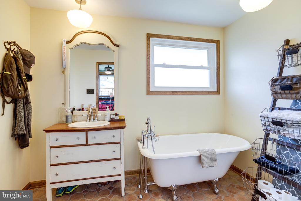 Bathroom with a freestanding clawfoot tub beside a dresser-style vanity and wood-trimmed window.