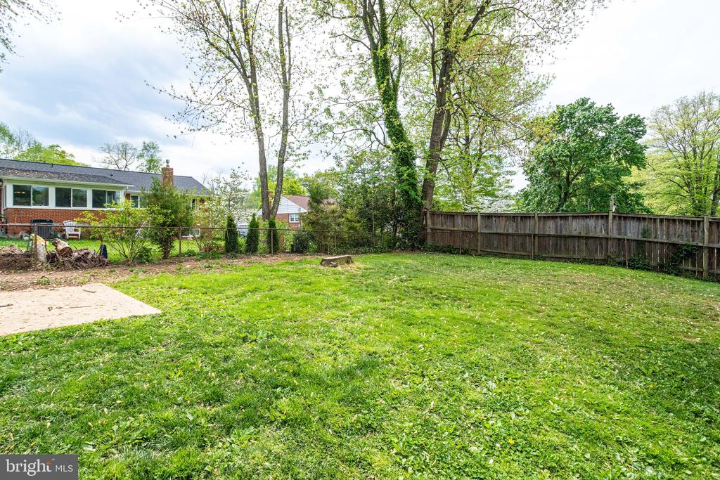 Grassy backyard with mature trees, a wooden fence, and a small patio.
