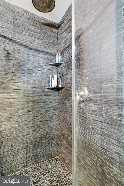 Walk-in shower with gray stone tile, a pebble floor, and glass enclosure.