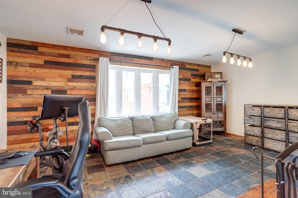 Furnished recreation room with a gray sofa, reclaimed-wood accent wall, slate floor, and exercise bike.