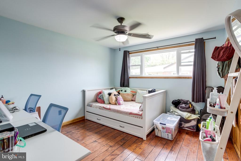 Bedroom with a white daybed beneath a wide window and a desk in the foreground.