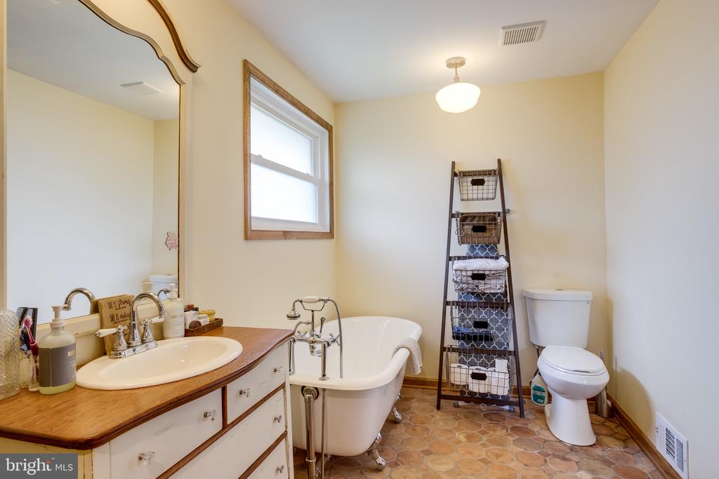Bathroom with a wood-top vanity, freestanding clawfoot tub, and patterned tile floor.