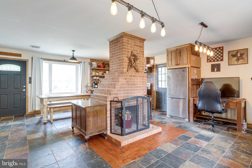 Kitchen and dining area with a central brick fireplace, tiled floor, and wooden cabinetry.