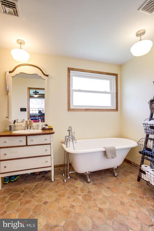 Bathroom with a freestanding clawfoot tub, wood-trimmed mirror, and tan geometric tile floor.