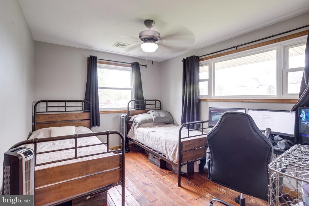 Bedroom with two wooden single beds, hardwood floors, and a desk beside large windows.