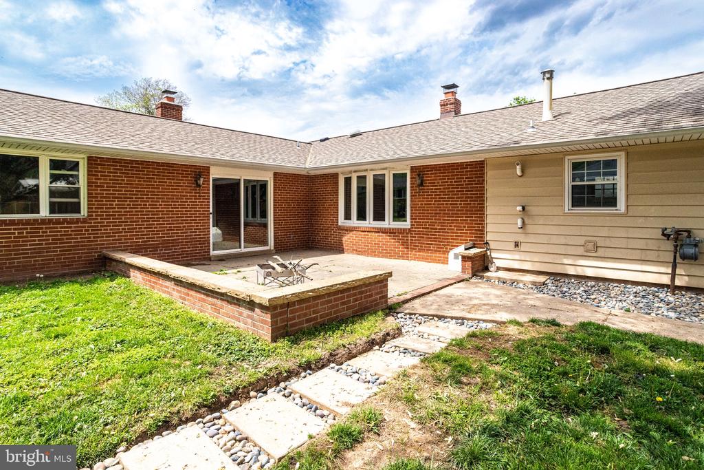 Brick home’s rear patio with sliding glass doors and stepping stones across the grassy yard.