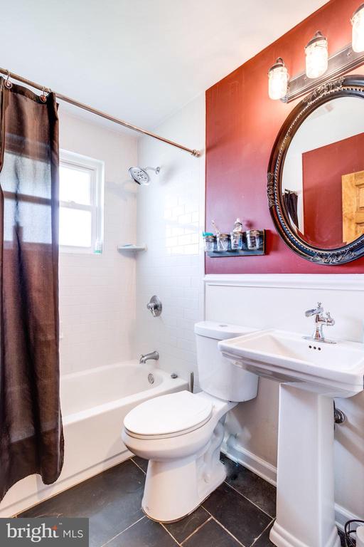 Bathroom with a white tub, dark shower curtain, pedestal sink, and ornate mirror on a red wall.