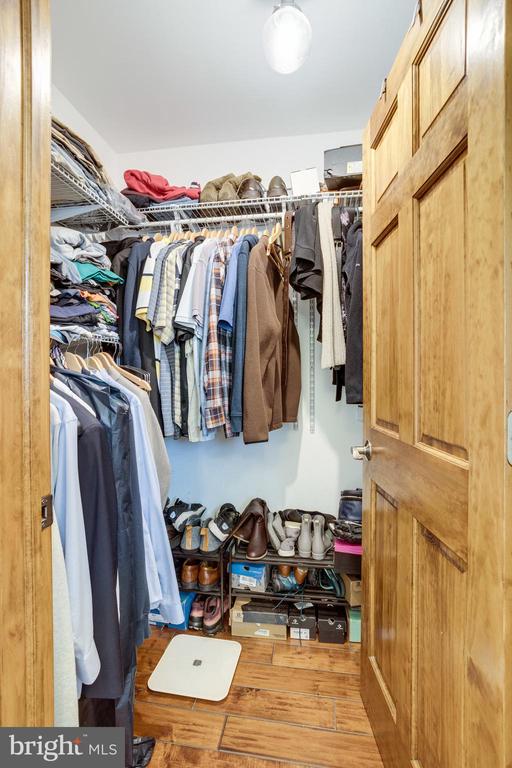 Walk-in closet with hanging clothes, shelves, and rows of shoes.
