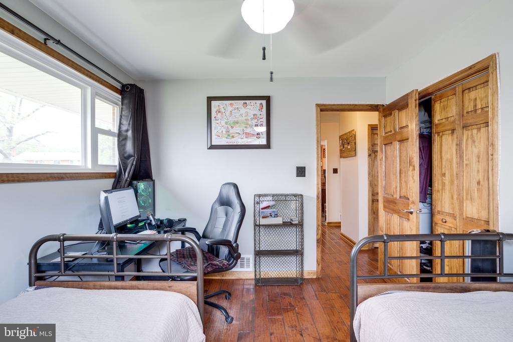 Bedroom with two beds, a computer desk by the window, and open wooden closet doors.