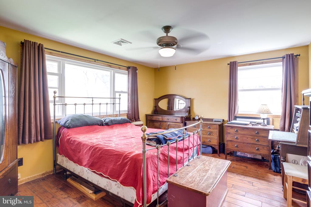 Bedroom with a red-covered metal bed, yellow walls, hardwood floors, and mauve curtains.