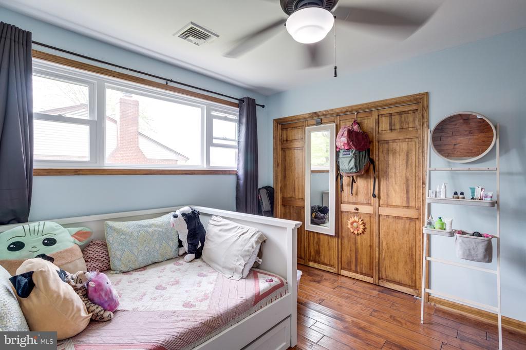 Bedroom with a white bed, plush toys, wide window, and wooden closet doors.