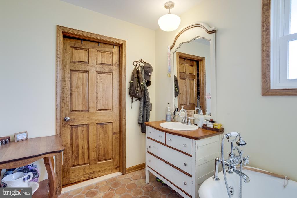 Bathroom with a wood-paneled door, dresser-style vanity, ornate mirror, and bathtub with chrome fixtures.