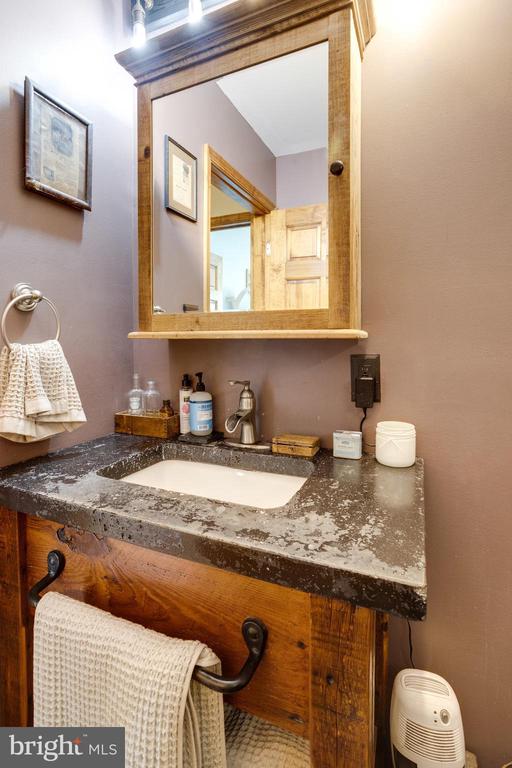 Bathroom vanity with a mottled dark countertop, rustic wood cabinet, and large wood-framed mirror.