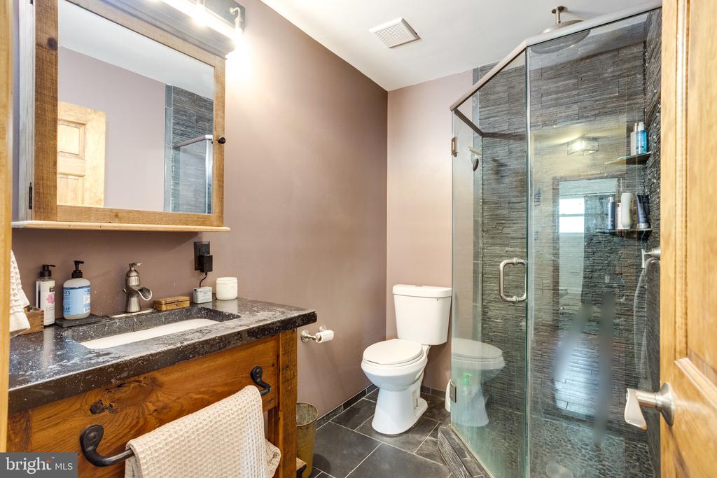 Bathroom with a rustic wood vanity and glass-enclosed dark-tile shower.