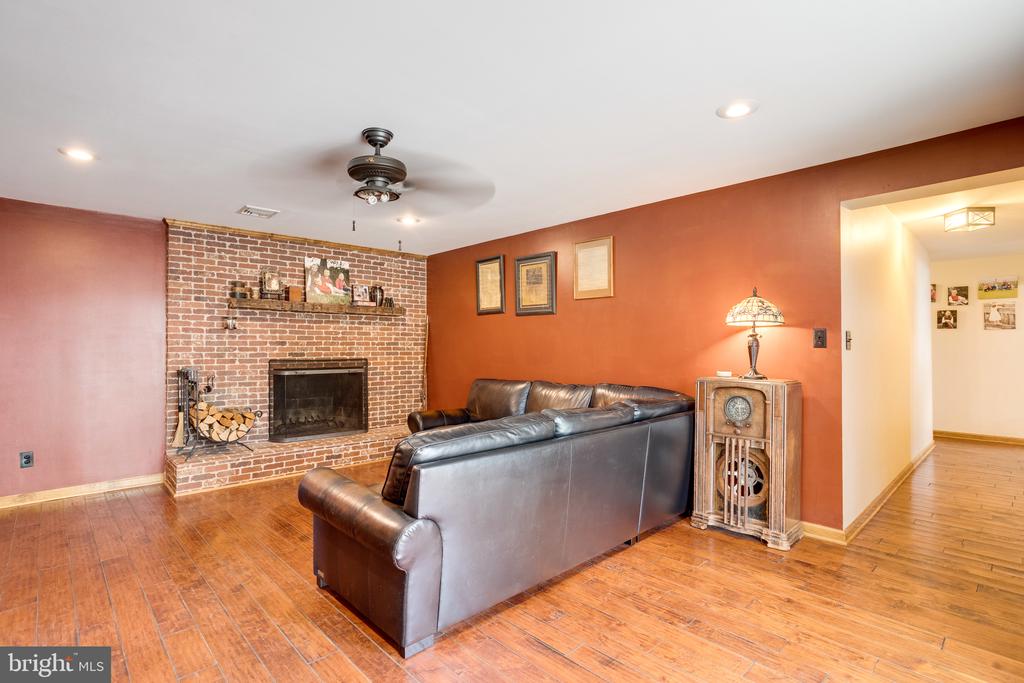 Living room with a brick fireplace, leather sectional, and warm-toned hardwood floors.