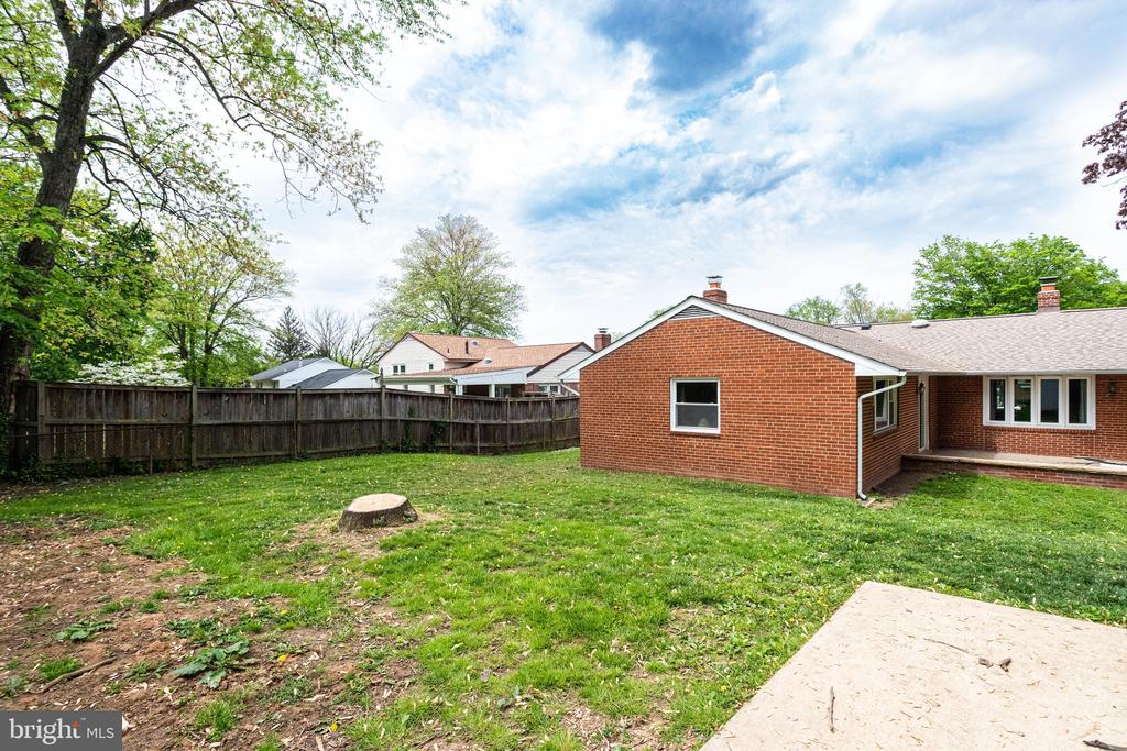 Red-brick home behind a grassy backyard with a wooden fence and concrete patio.