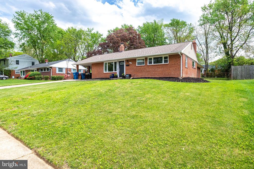 Red-brick single-story home with a broad front lawn and mature trees.