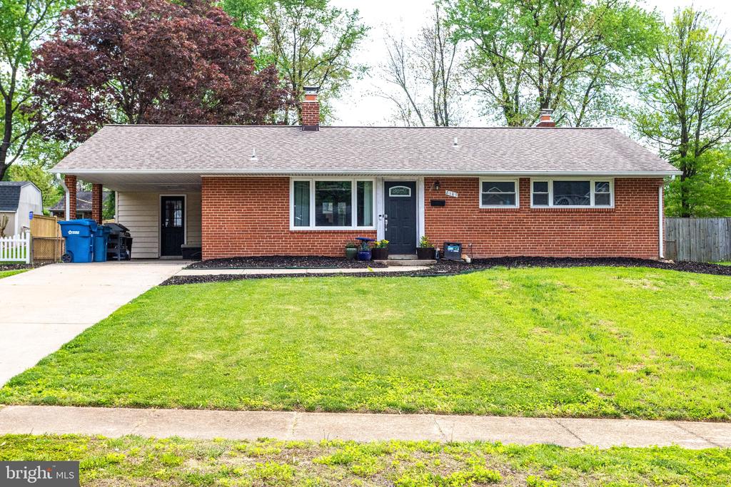Single-story red brick home with a covered carport, concrete driveway, and broad front lawn.