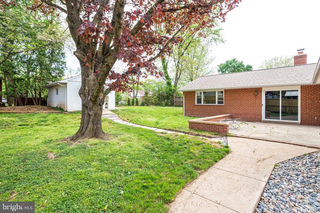 Brick home and patio beside a large tree in a grassy backyard.