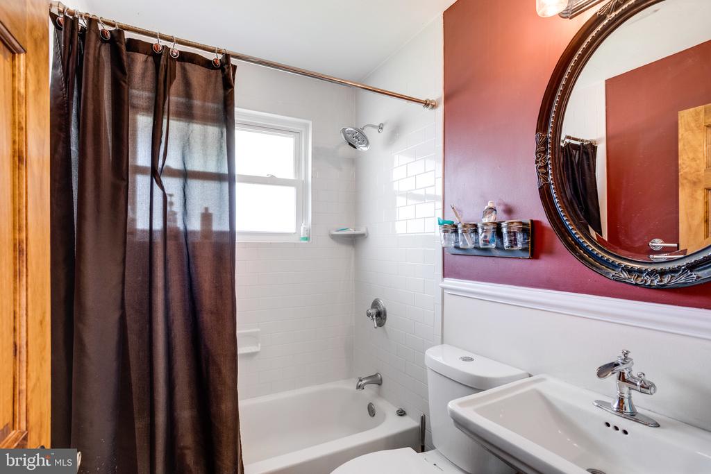 Bathroom with a white tiled tub and shower, dark curtain, and burgundy wall with an ornate mirror.