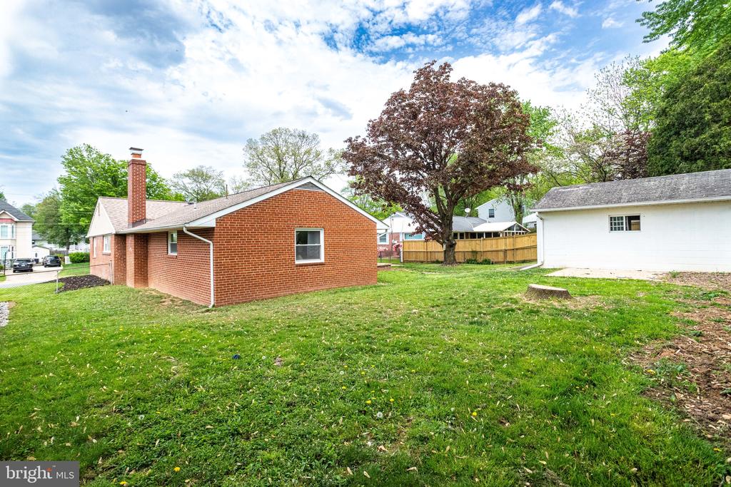 Rear of a red brick ranch home across a grassy yard, with a detached white garage and mature trees.