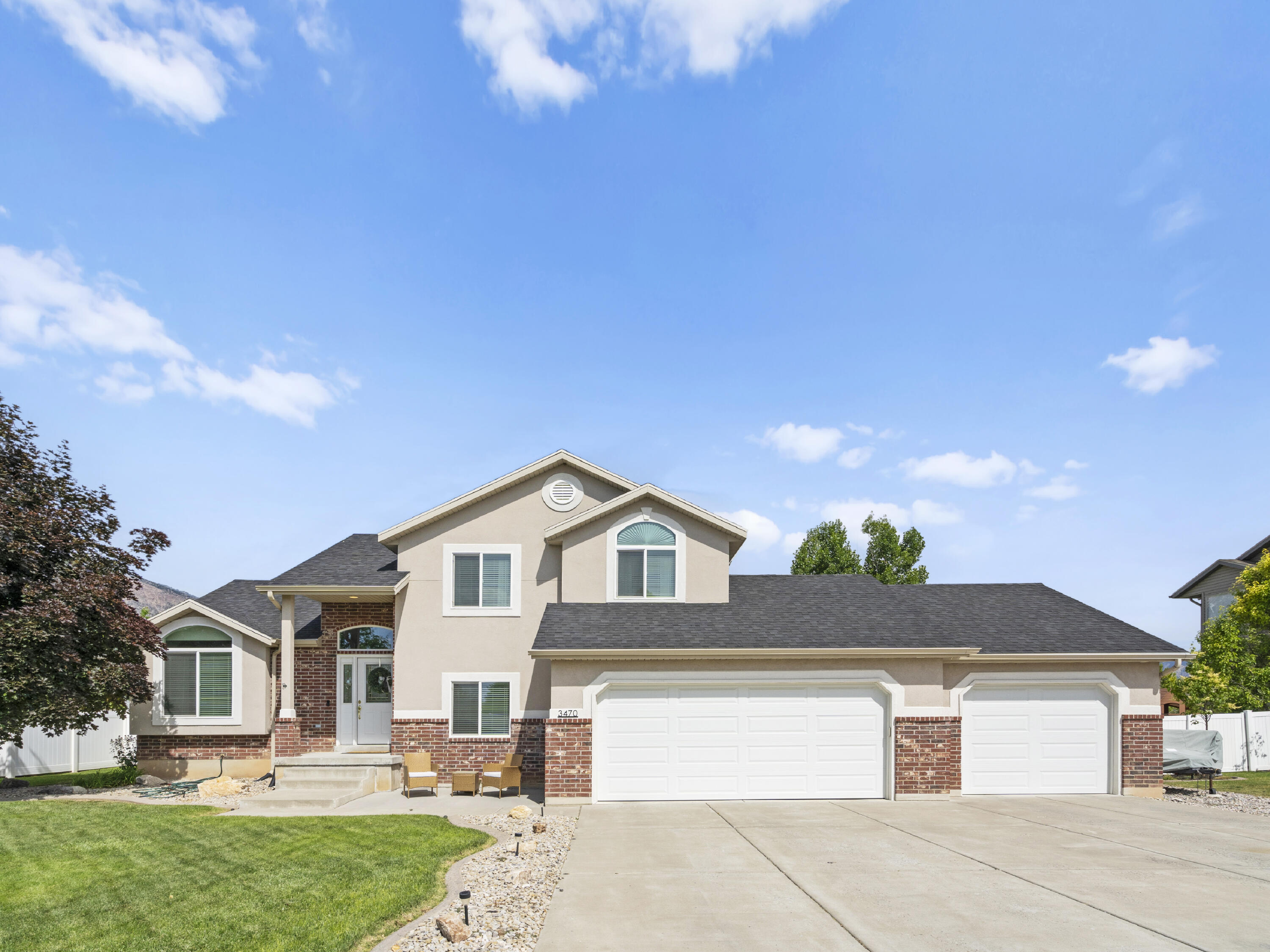 Two-story beige stucco and brick home with a three-car garage and broad concrete driveway.