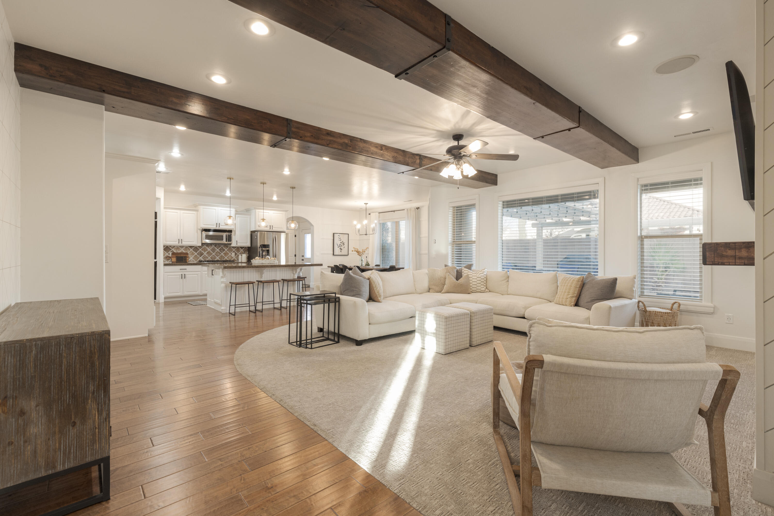 Open-plan living room with a cream sectional, exposed wood ceiling beams, and kitchen beyond.