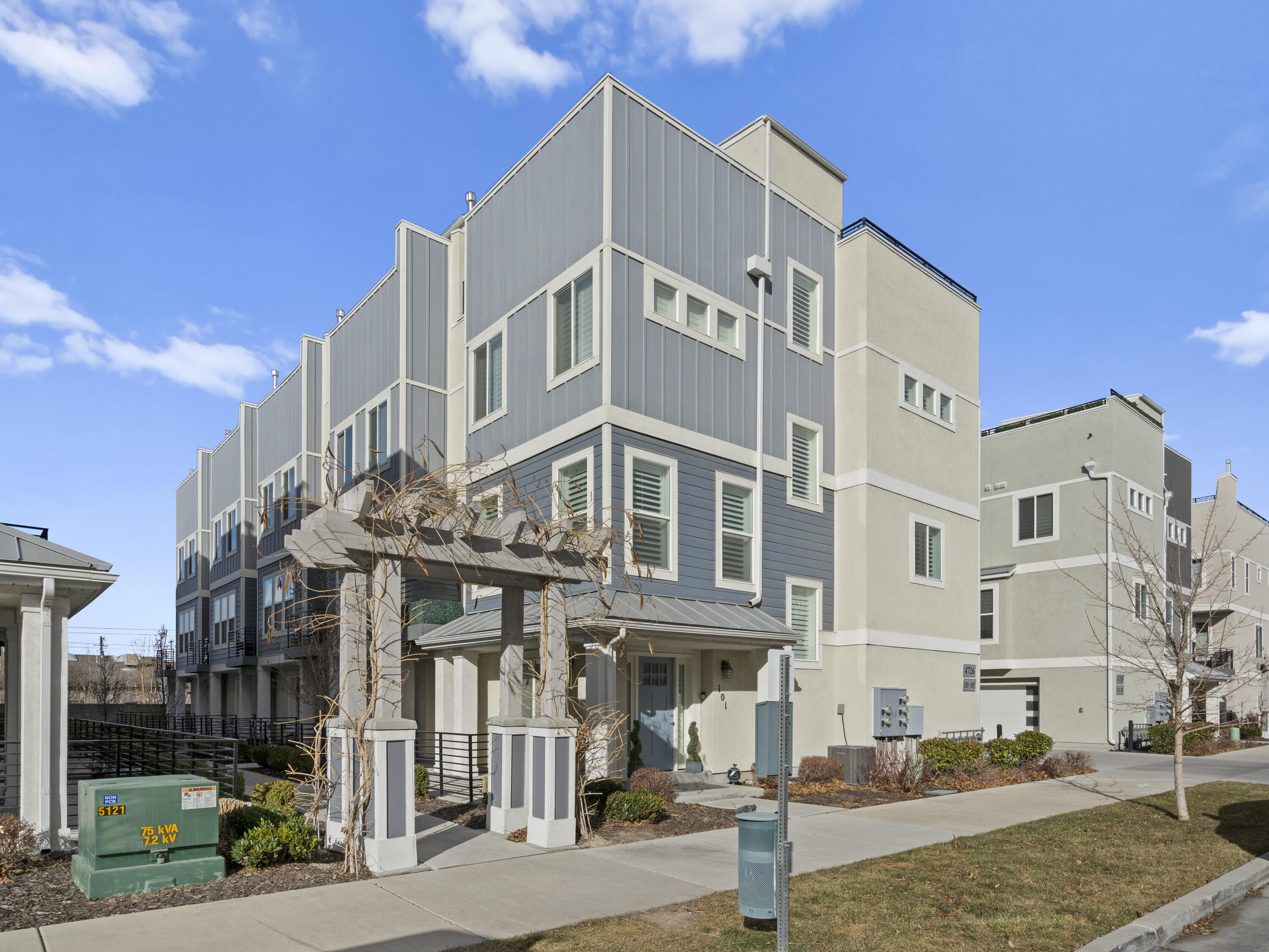 Modern gray and cream townhomes with large windows and a vine-covered pergola at the entrance.