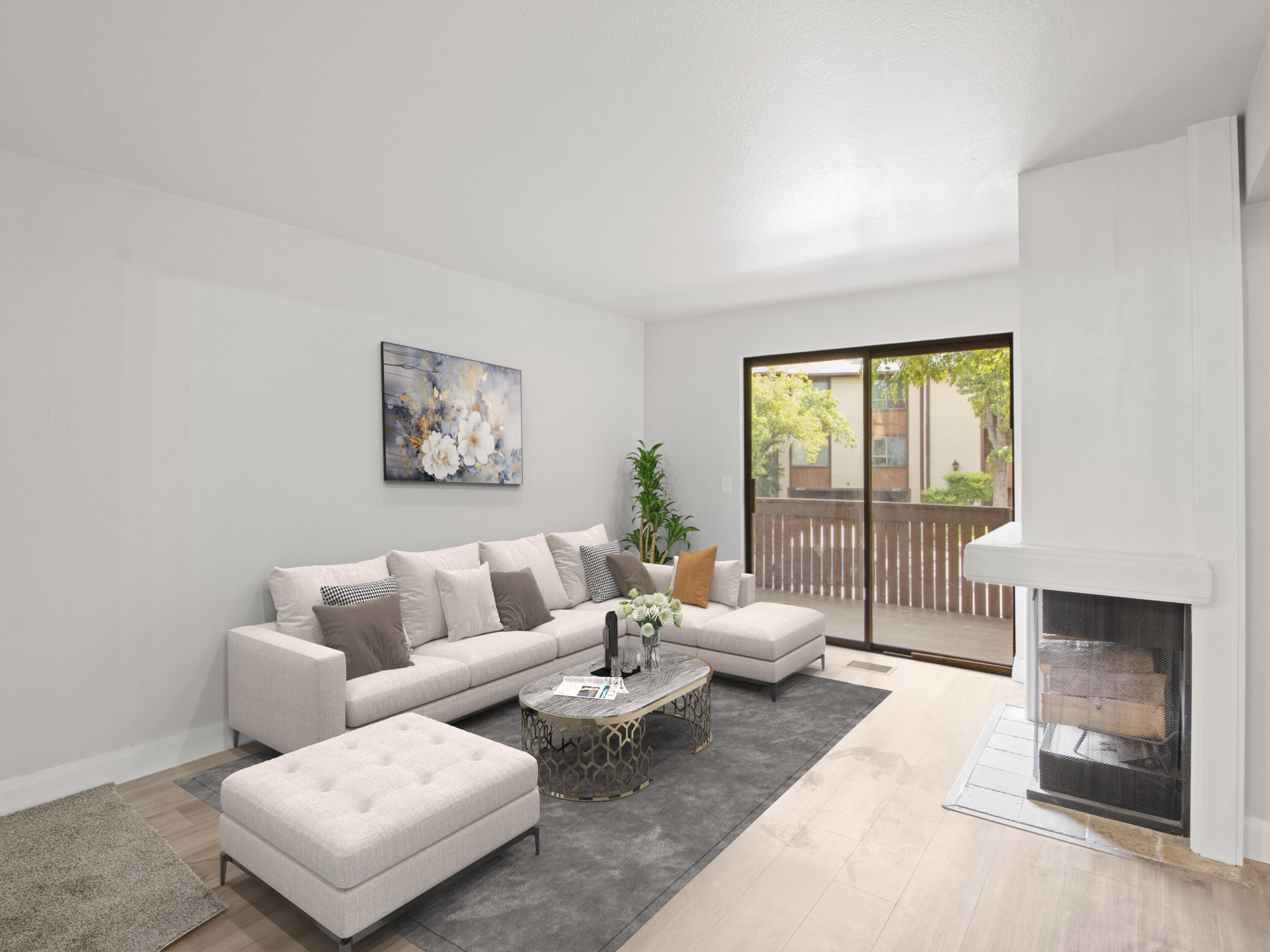Staged living room with a light sectional, modern fireplace, and sliding doors to a leafy balcony.