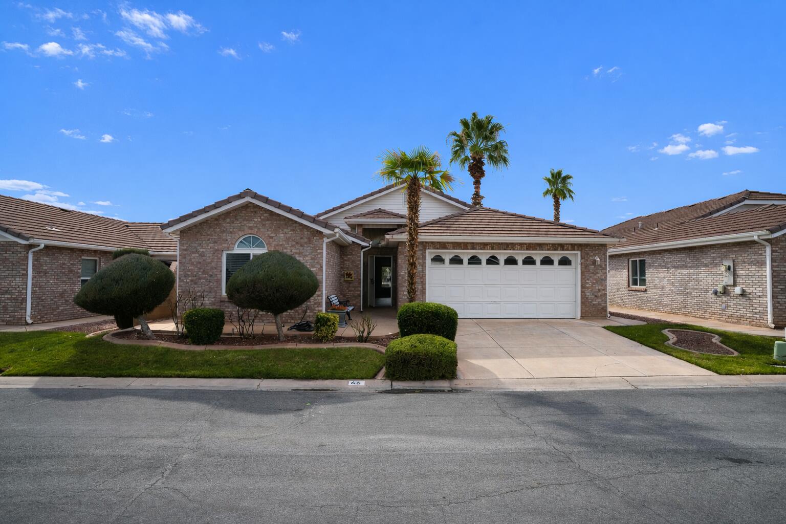 Brick house with an attached two-car garage, trimmed shrubs, and palm trees in the front yard.