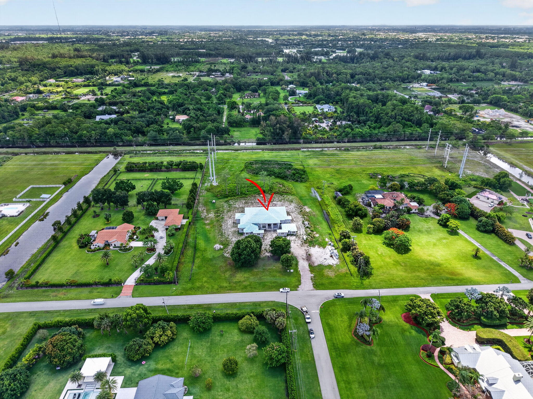 Aerial view of a house on a cleared lot, marked with a red arrow, among neighboring homes.