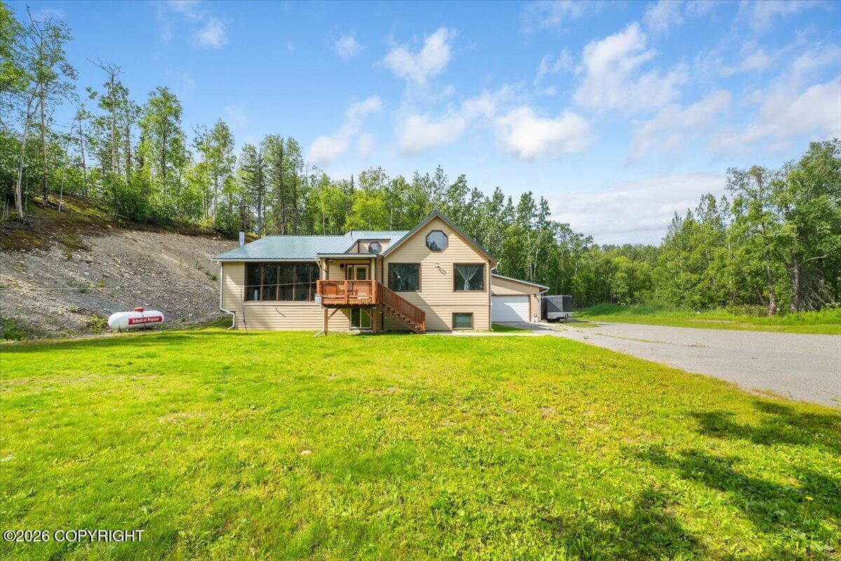 Tan two-story house with a screened porch, raised deck, and attached garage on a grassy wooded lot.