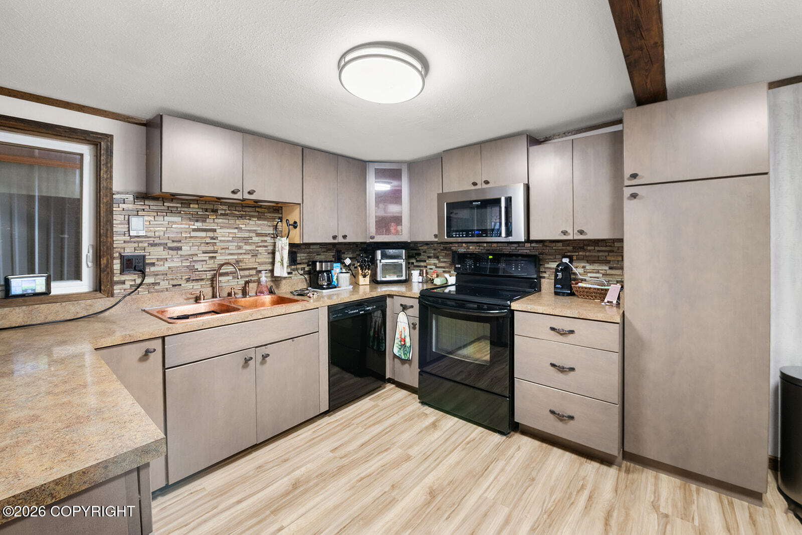 Kitchen with pale cabinets, patterned tile backsplash, copper-colored sink, and black appliances.