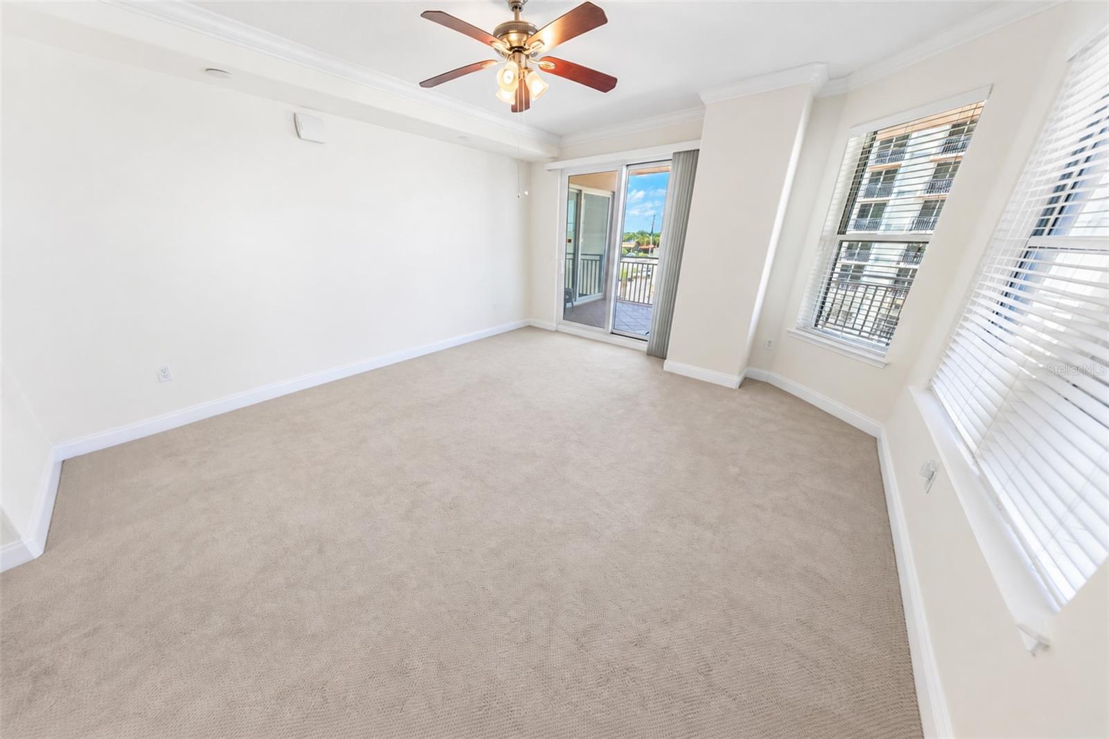 Empty carpeted condo room with a ceiling fan and sliding glass door to a balcony.